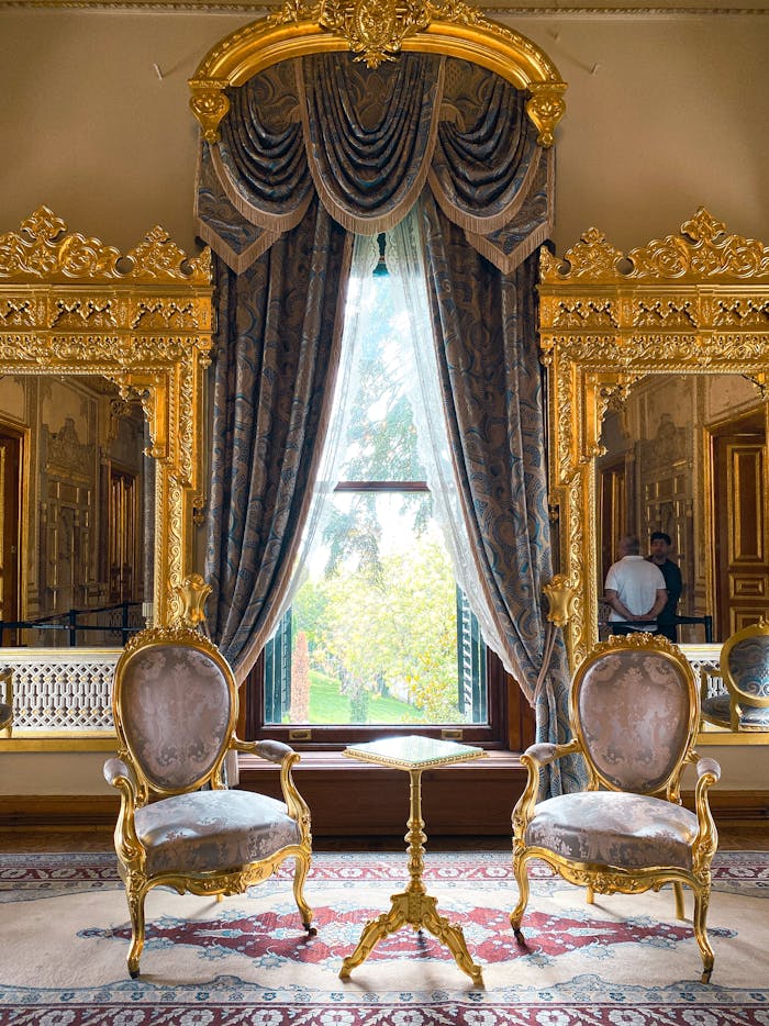الجمال للأثاث ( ورشة ربيع احمد نعيم ) Elegant room with opulent gold decor and vintage chairs overlooking lush greenery.